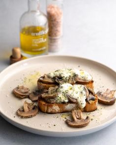 a white plate topped with toast covered in mushrooms next to a bottle of mustard and seasoning