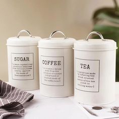 three white canisters with labels on them sitting on a table next to a napkin