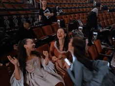 two women laughing in an empty theater with other people around them and one woman sitting on the floor