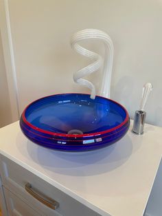 a blue and red bowl sitting on top of a white counter next to a silver faucet