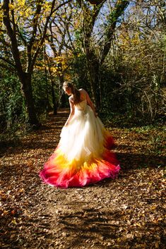 a woman in a colorful dress is walking through the woods with leaves on the ground