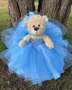 a teddy bear wearing a blue dress sitting in the grass next to two tree trunks