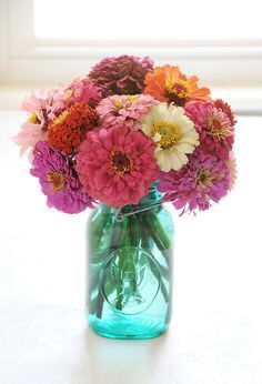 a glass vase filled with colorful flowers on top of a white table next to a window