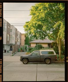 a truck parked on the side of a street next to a tree and building with lots of windows