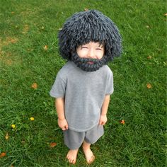 a young boy wearing a fake wig and beard in the grass with his hands on his hips