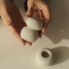 two hands holding three white rocks on top of a table