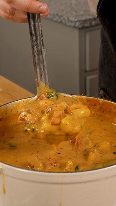 a person is holding a ladle over a pot full of food on the counter