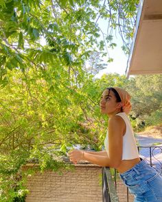 a woman standing on a balcony next to a tree and looking up at the sky