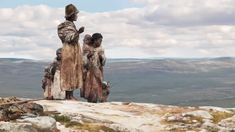 two people standing on top of a rocky hill with mountains in the backgroud