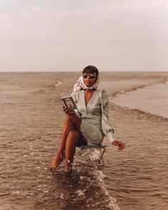 a woman is sitting on a chair in the water with her legs crossed and wearing sunglasses