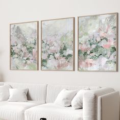 three paintings hang on the wall above a white couch