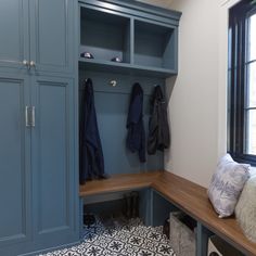 a blue bench with coat racks and pillows on it next to a black and white tile floor