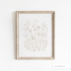 a white framed artwork hanging on the wall next to a wooden frame with flowers in it