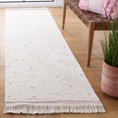 a white rug with pink polka dots on it next to a chair and potted plant