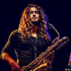 a man with long curly hair holding a saxophone in front of a microphone on stage