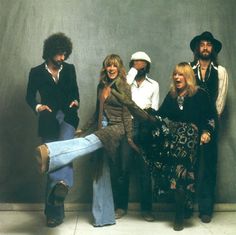 a group of people standing next to each other in front of a gray wall with their legs spread out