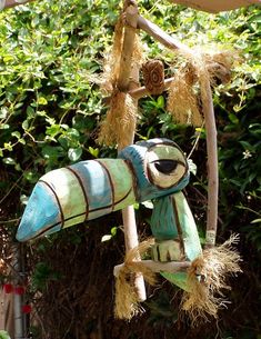 a blue and white bird hanging from a wooden pole in front of some bushes on a sunny day