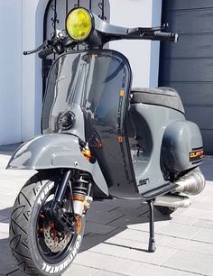 a grey scooter parked in front of a white building with a yellow light on it