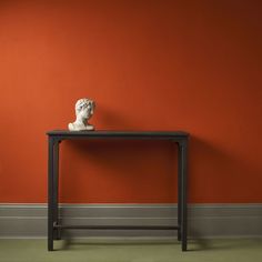 an orange wall with a black table and white busturine on top in front of it