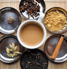 four bowls with different types of spices and coffee in them on a mat next to plates