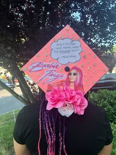 a woman wearing a pink graduation cap with braids and flowers on her head, in front of a tree