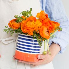 a person holding a blue and white striped vase with orange flowers in it's center