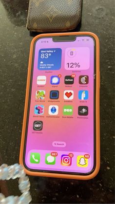 an orange and pink cell phone sitting on top of a table next to a wallet