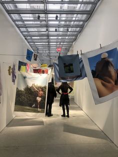 two people standing in an art gallery looking at pictures hanging on the wall and down