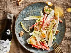 a blue plate topped with salad next to a bottle of wine