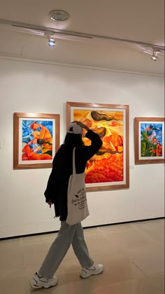 a woman walking past paintings in an art gallery