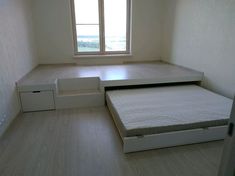 an empty room with a bed, drawers and a window in the corner is shown