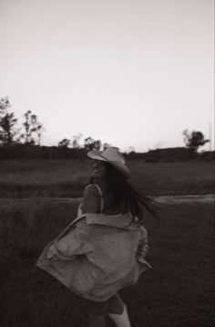 black and white photograph of a woman walking through a field with a hat on her head