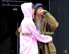 two people standing next to each other with microphones in their hands and one person wearing a pink hoodie