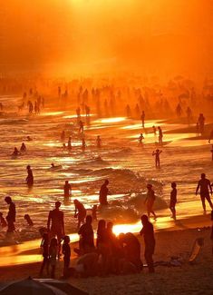 many people are standing on the beach at sunset or sunrise, with bright orange and yellow colors