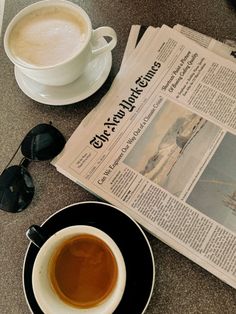 a cup of coffee sitting on top of a black saucer next to a newspaper