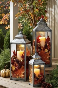 two lanterns sitting on top of a porch next to trees and leaves with candles in them