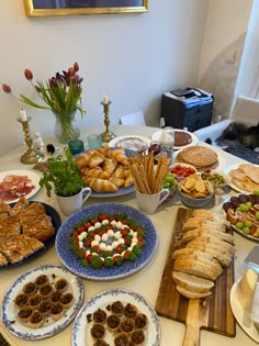 a table full of food and breads on plates with flowers in vases next to it