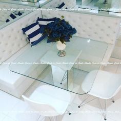 a glass table with white chairs and blue flowers on it in front of a mirror