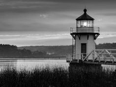 a black and white photo of a light house in the middle of water with grass around it