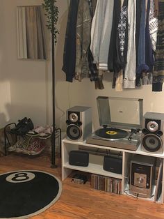 there is a record player in the corner of this room with clothes hanging on the rack