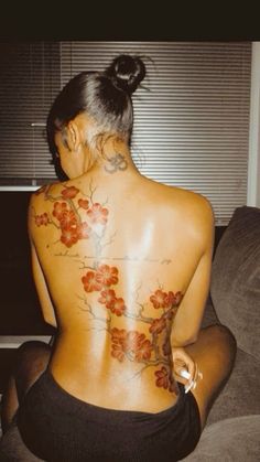 a woman with tattoos on her back sitting on a couch in front of a window