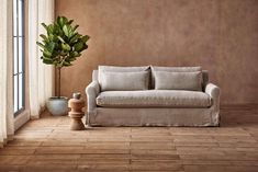 a living room with a couch, potted plant and large window in it's corner