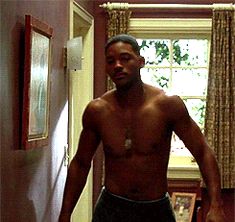 a man without a shirt standing in a hallway next to a window with curtains on the windowsill