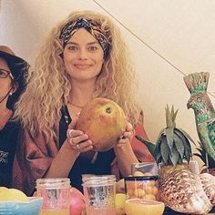 two women sitting at a table with fruit and drinks in front of them, one holding an apple