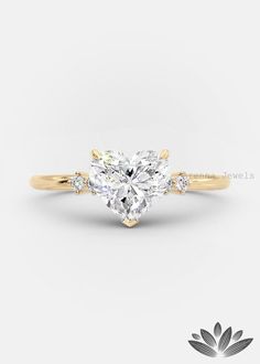 a heart shaped diamond engagement ring with three stones on the band and side stones in yellow gold