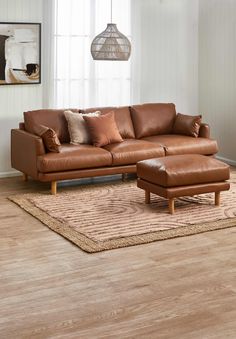 a brown leather couch sitting on top of a wooden floor next to a rug in front of a window