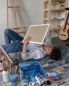 a woman laying on the floor holding up a painting