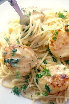 a white plate topped with pasta and meat covered in sauce, garnished with parsley