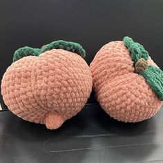 two crocheted peaches sitting on top of a car seat cover with green leaves