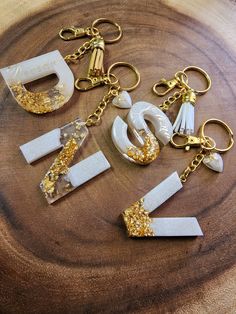 four different key chains with gold glitter on them sitting on a wooden surface, one is shaped like an arrow and the other has letters that spell out